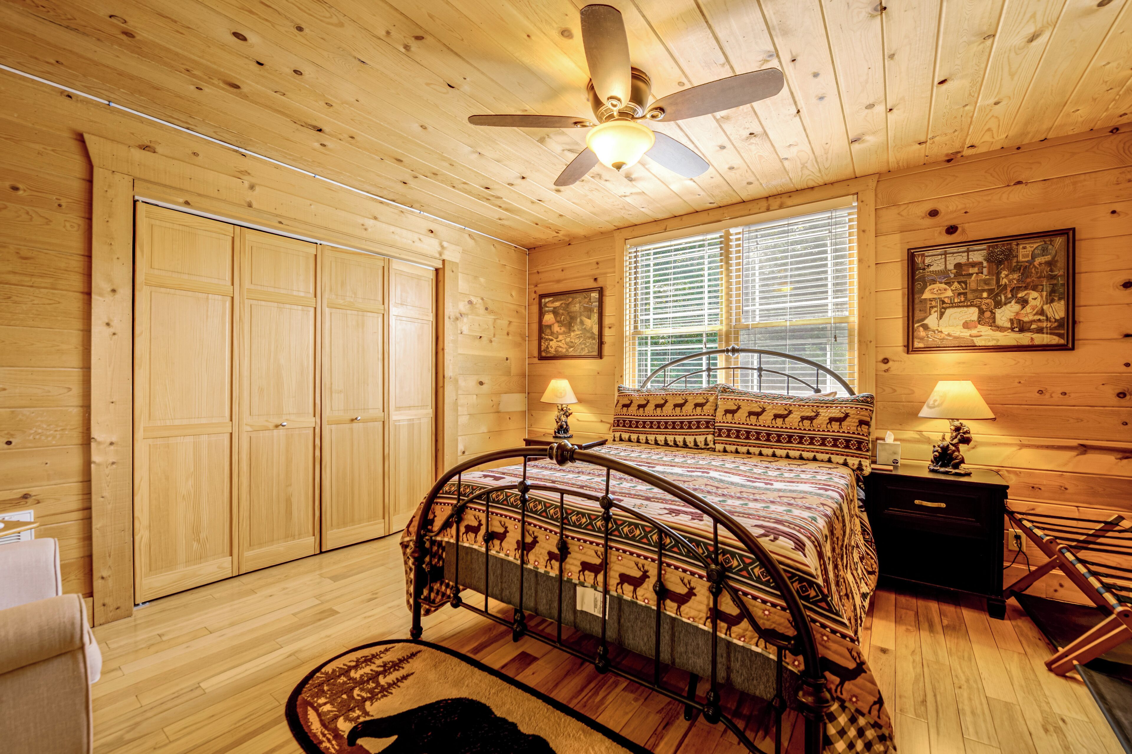 Una habitación con paneles de madera, una cama, un ventilador de techo, una ventana con persianas y una puerta.