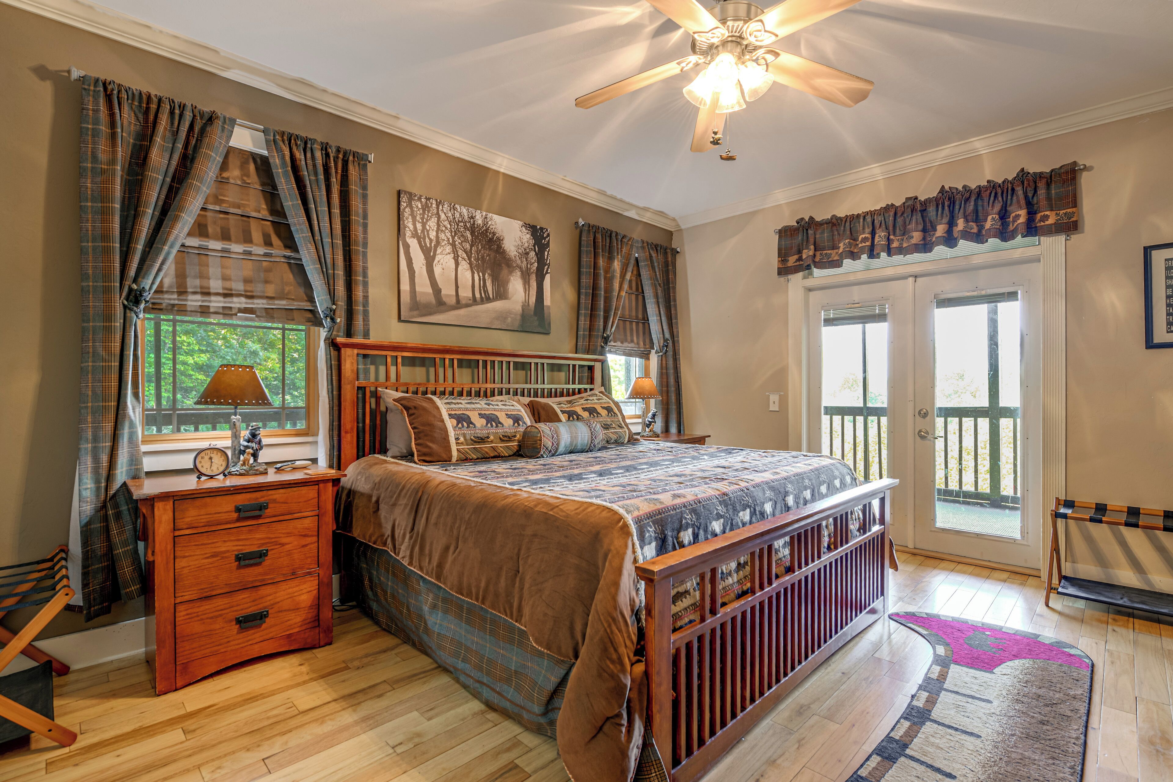 A bedroom with a wooden bed, a nightstand, a desk, a chair, a ceiling fan, and a window with curtains.