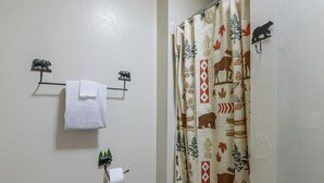 Un baño con toallero, dispensador de papel higiénico y cortina de ducha con motivos naturales.