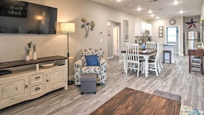 A spacious living area with a wooden floor, a sofa, a TV mounted on the wall, and a dining area with a table and chairs. - 4BR Sleeps 10 Game Room 4 Mi to SDC (Branson)