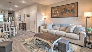A living room with a beige sofa, a wooden coffee table, and a rug. There is a ceiling fan, a wall-mounted lamp, and a framed map on the wall. - 4BR Sleeps 10 Game Room 4 Mi to SDC (Branson)