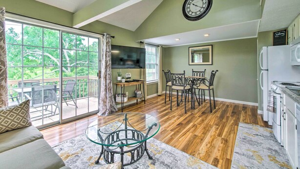 A spacious living room with a glass coffee table, a dining area with chairs, a kitchen with appliances, and a large window with a view of greenery. - Branson Escape: 9 Mi to Silver Dollar City! (Branson)
