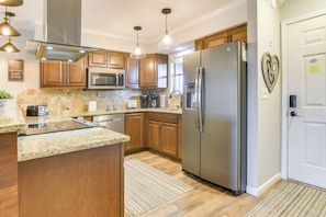 A modern kitchen with wooden cabinets, stainless steel appliances, granite countertops, and pendant lighting.