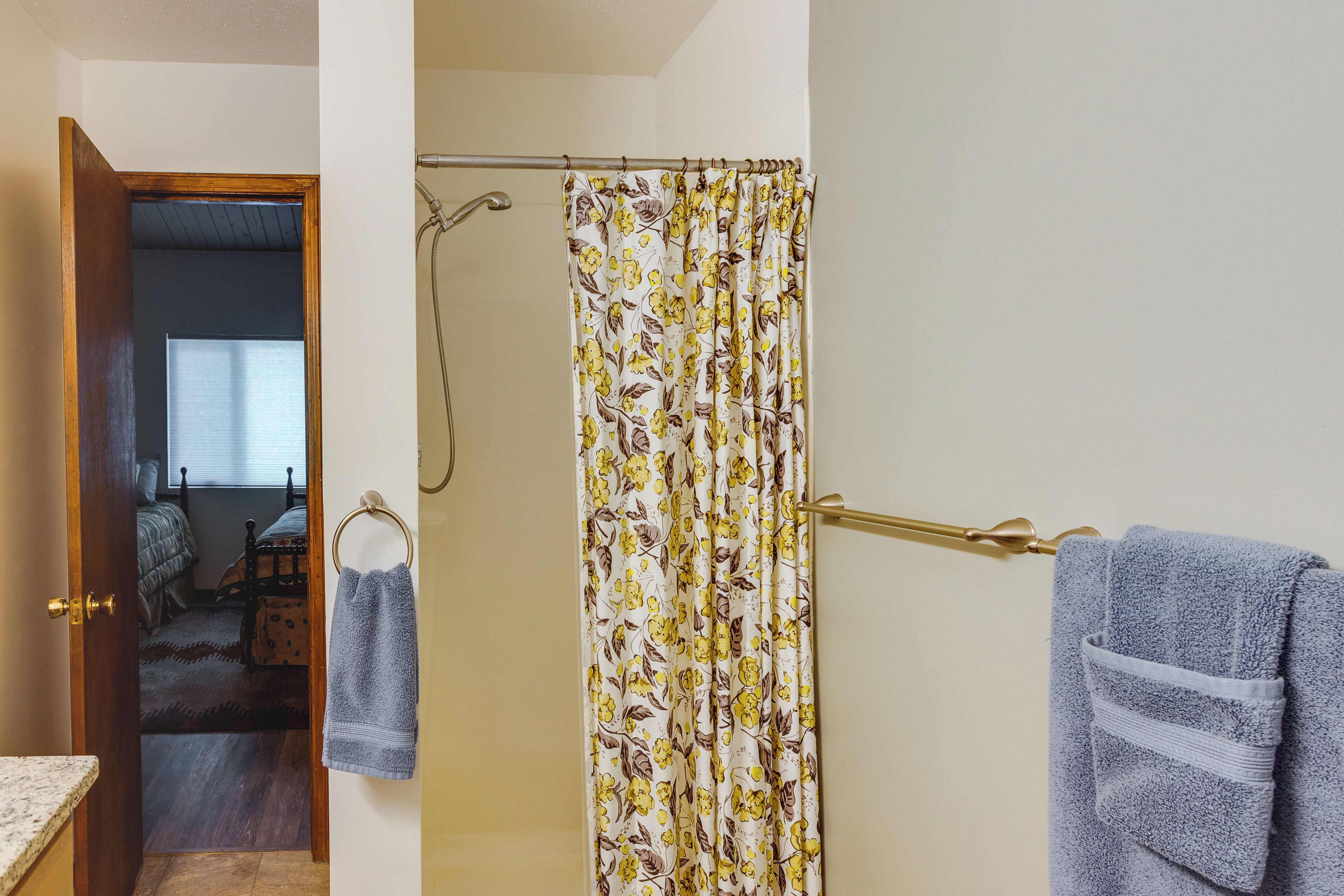 Une salle de bain avec un rideau de douche, un porte-serviettes et une porte visible donnant sur une chambre.
