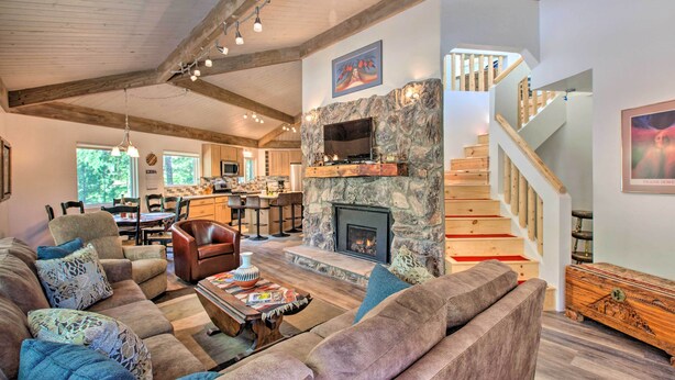 A spacious living room with a stone fireplace, wooden ceiling beams, and a staircase leading to an upper level. - Angel Fire Home w/ Deck ~ 3 Mi to Ski Resort! (Angel Fire)