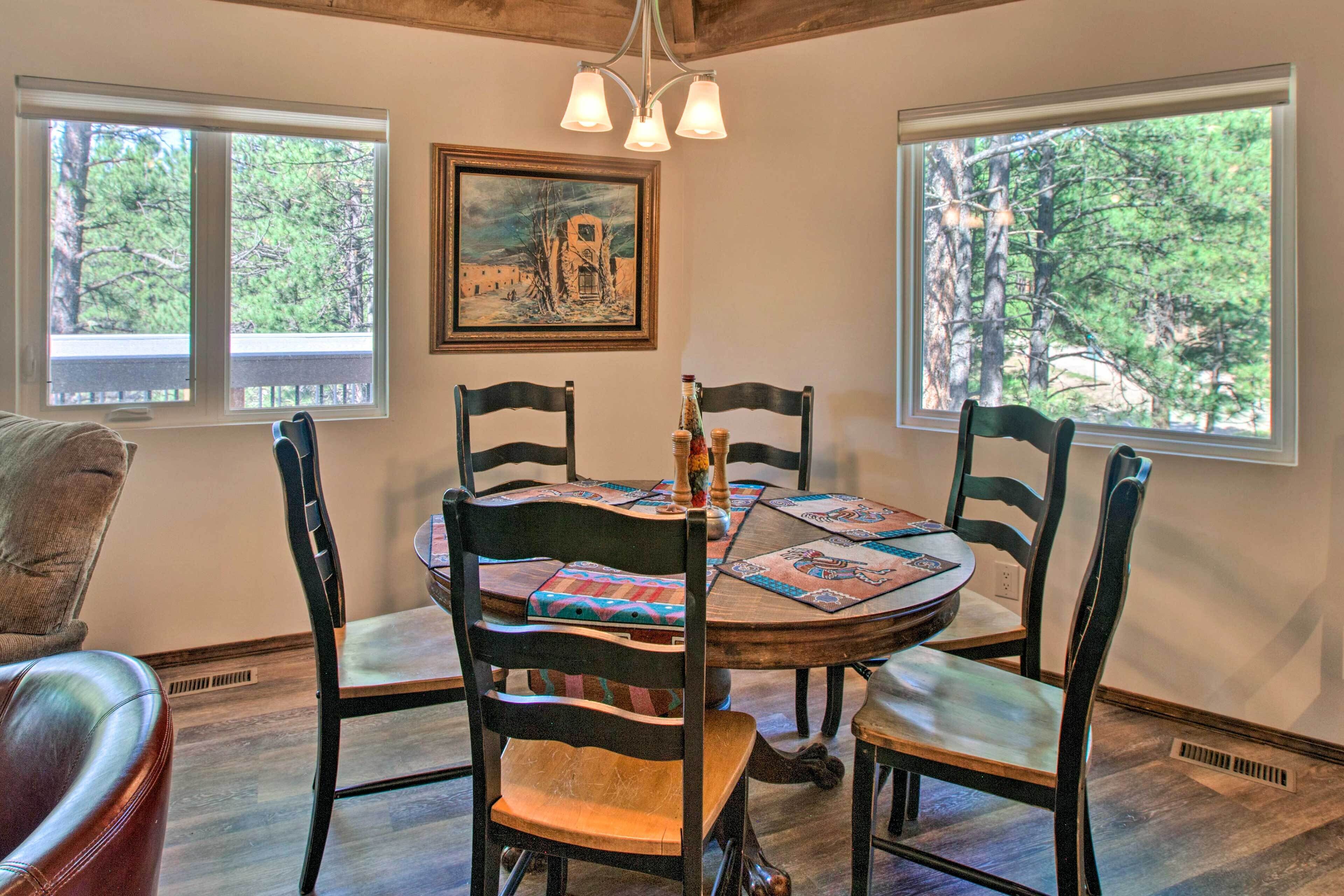 A dining area with a round table, four chairs, and a painting on the wall.