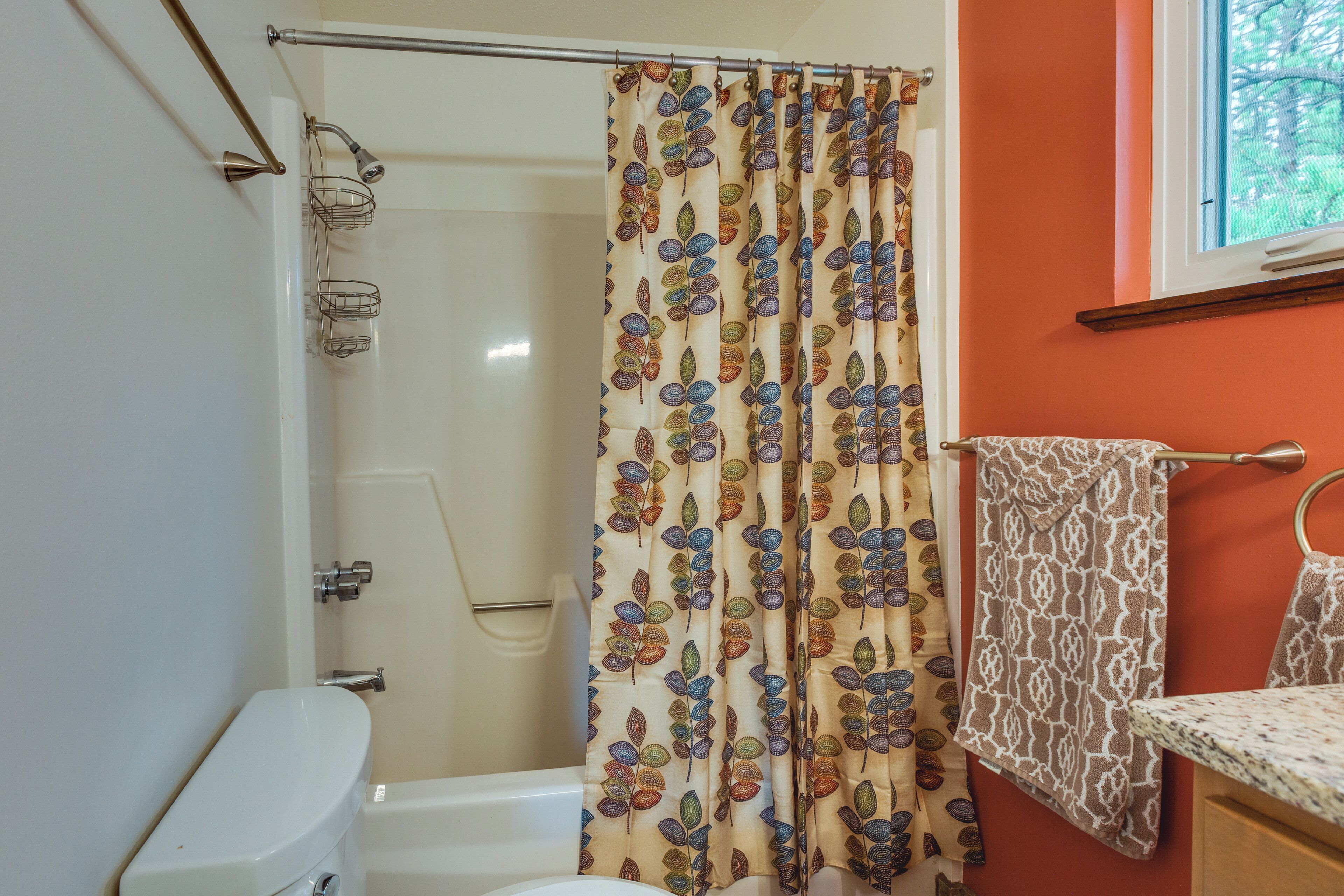 A bathroom with a shower curtain featuring a leaf pattern, a white toilet, and a towel rack with a patterned towel.
