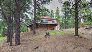 A two-story house with a balcony, surrounded by pine trees and a grassy area. - Angel Fire Home w/ Deck ~ 3 Mi to Ski Resort! (Angel Fire)