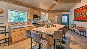 A spacious kitchen with wooden cabinets, a large island with bar stools, a microwave, and a refrigerator. - Angel Fire Home w/ Deck ~ 3 Mi to Ski Resort! (Angel Fire)
