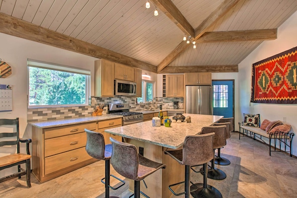 A kitchen with wooden cabinets, a central island with bar stools, a microwave, and a refrigerator.