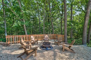 A deck with Adirondack chairs and a fire pit surrounded by gravel, set in a forested area. - Beautiful Bull Shoals Retreat w/ Lake View! (Bull Shoals)