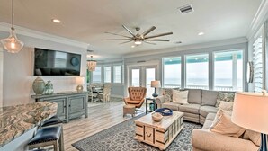A spacious living room with a large TV, comfortable seating, a ceiling fan, and large windows offering a view of the ocean. - Beachfront Retreat: 16 Mi to Dtwn Freeport! (Freeport)