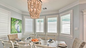 A dining room with a wooden table set for six, surrounded by wicker chairs, with a painting of a bird on the wall and a chandelier above. - Beachfront Retreat: 16 Mi to Dtwn Freeport! (Freeport)