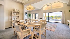 Un vaste espace dédié à la salle à manger, avec une table à plateau de verre et des chaises rembourrées, un lustre, et une vue sur l’extérieur grâce à de grandes fenêtres.