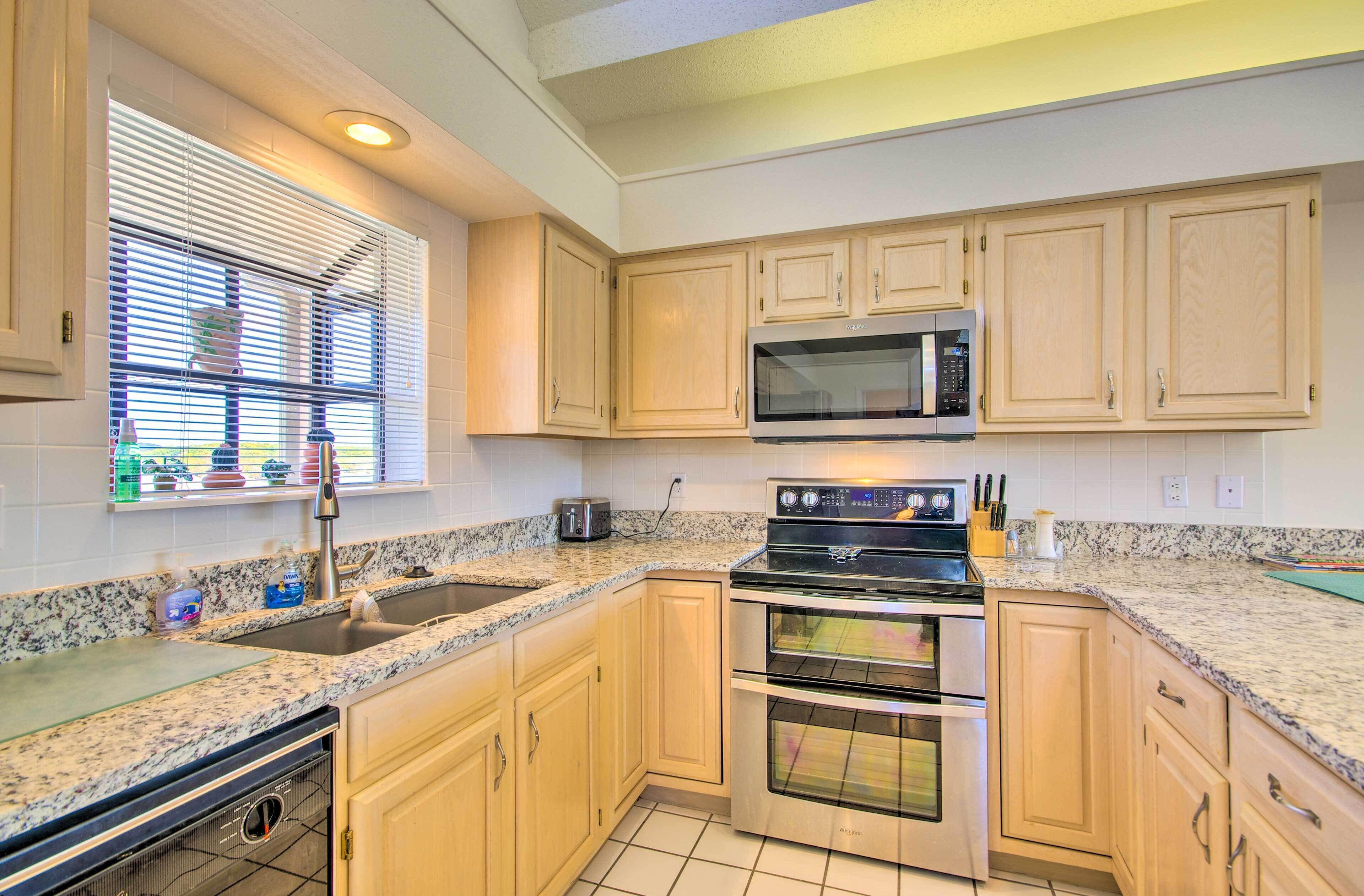 A kitchen with granite countertops, stainless steel appliances, and light wood cabinets.