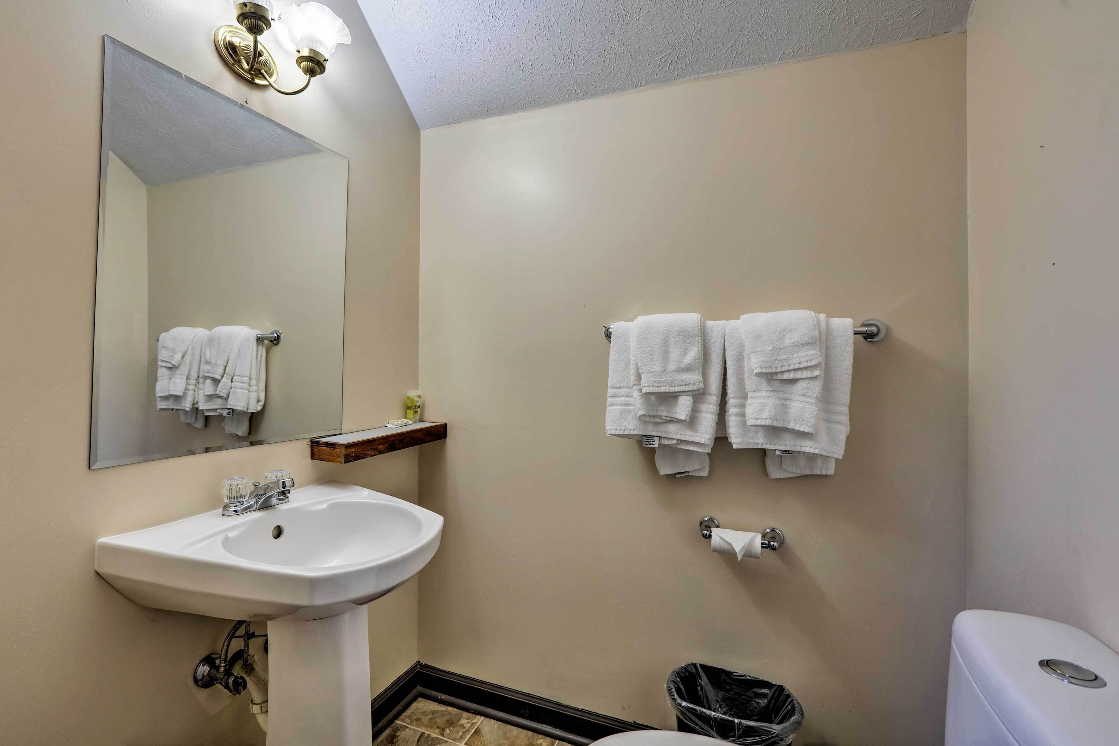 A bathroom with a sink, mirror, two towel racks, a toilet, and a trash bin.