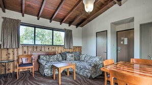 A cozy room with a wooden ceiling, a large window with curtains, a patterned sofa, a wooden table, and a dining area with chairs. - Burkesville Apt w/ Deck, Views & Pool Access! (Burkesville)