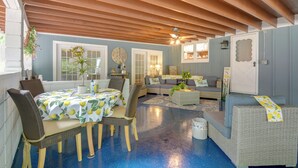 Un salon chaleureux avec un coin repas, comprenant des meubles en osier, un ventilateur de plafond et un sol bleu.