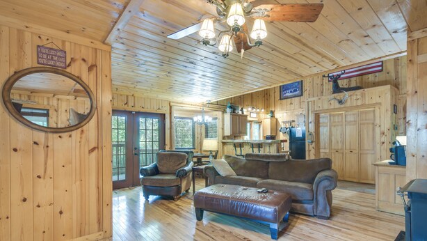 A wooden cabin interior with a dining area, kitchen, and seating with a fireplace.