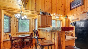 A wooden cabin interior with a dining area, bar stools, a refrigerator, and wooden cabinets.