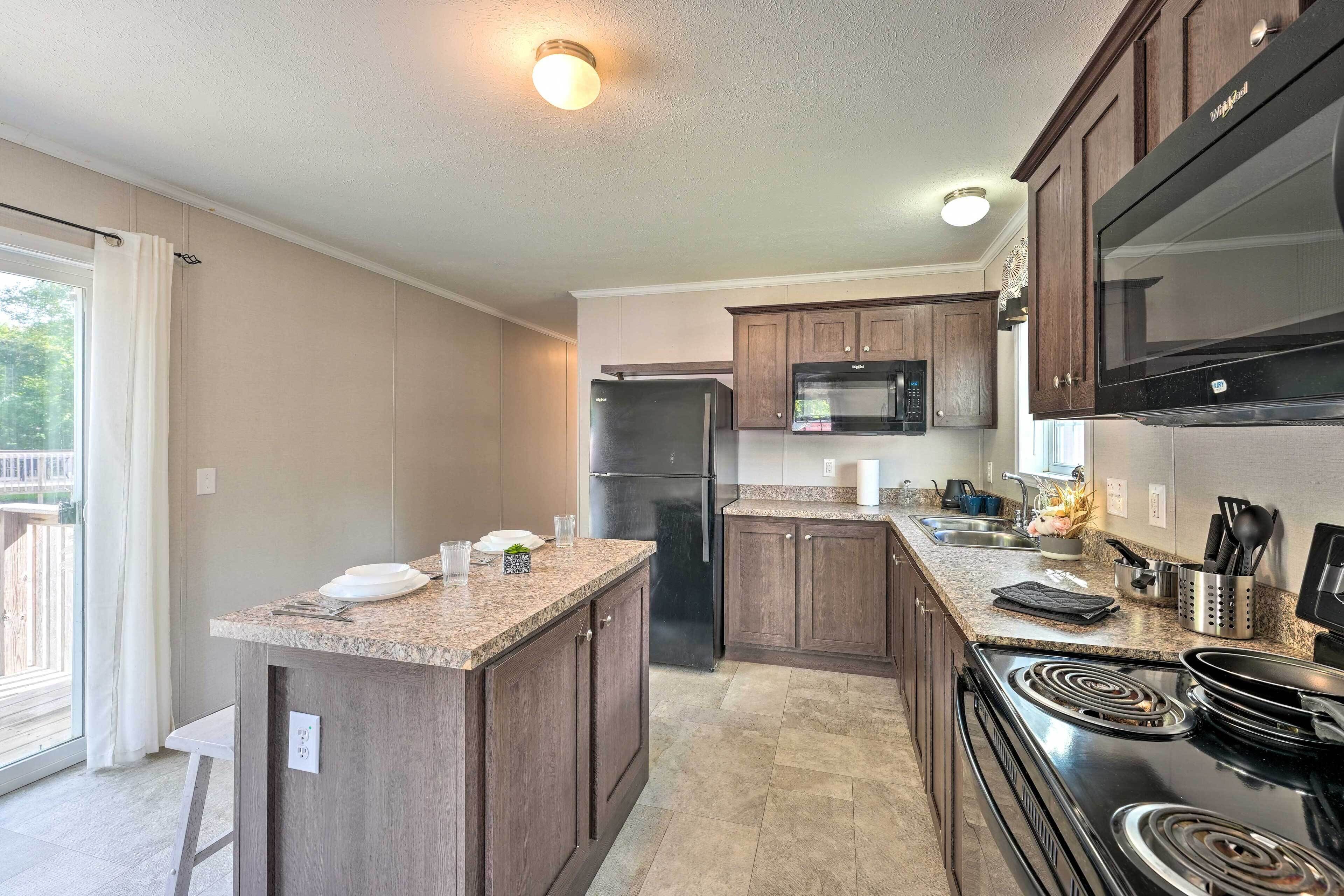 A modern kitchen with granite countertops, dark wood cabinets, a black refrigerator, a microwave, and a stove.