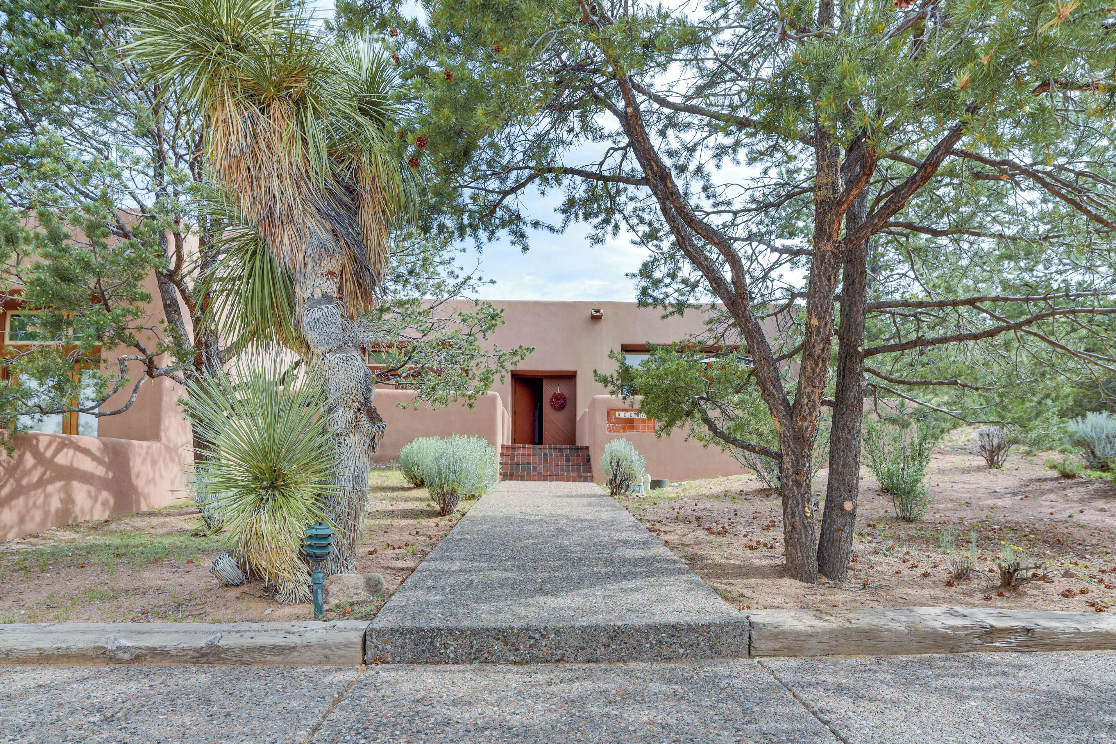 A pathway leading to a building with a red door, surrounded by various desert plants and trees.