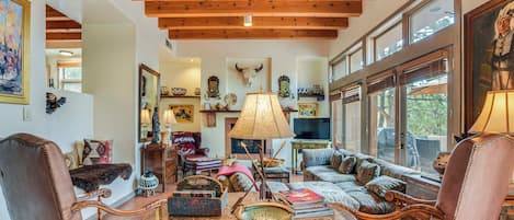 A spacious living room with a high wooden ceiling, comfortable seating, a fireplace, and a large window.