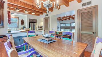 A spacious dining area with a wooden table and colorful chairs, a chandelier, and wooden beams on the ceiling.