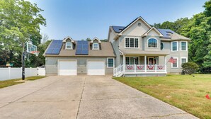 Une maison à deux étages dotée de panneaux solaires, d’un garage et d’un porche avant décoré d’un drapeau.