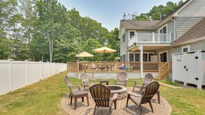 Une terrasse à l’arrière de la maison, avec des fauteuils Adirondack, un foyer et une plateforme en bois.