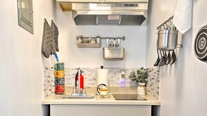 A kitchen with a stainless steel range hood, a hanging pot rack, and a coffee station. - Central Elmont Studio w/ Great Outdoor Space! (Elmont)