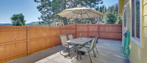 An outdoor patio with a table and chairs, a wooden fence, and a view of trees and hills.