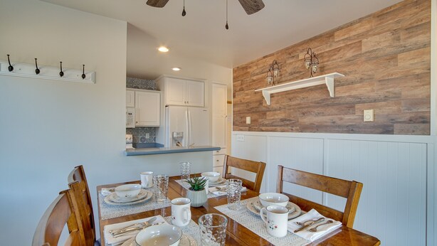 A dining area with a wooden table set for four, white chairs, and a kitchen in the background. - Charming Cle Elum Home w/ Patio: 5 Mi to Dtwn! (Cle Elum)