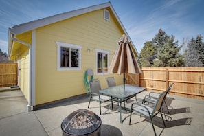 A yellow house with a patio, a table, chairs, a fire pit, and a wooden fence.