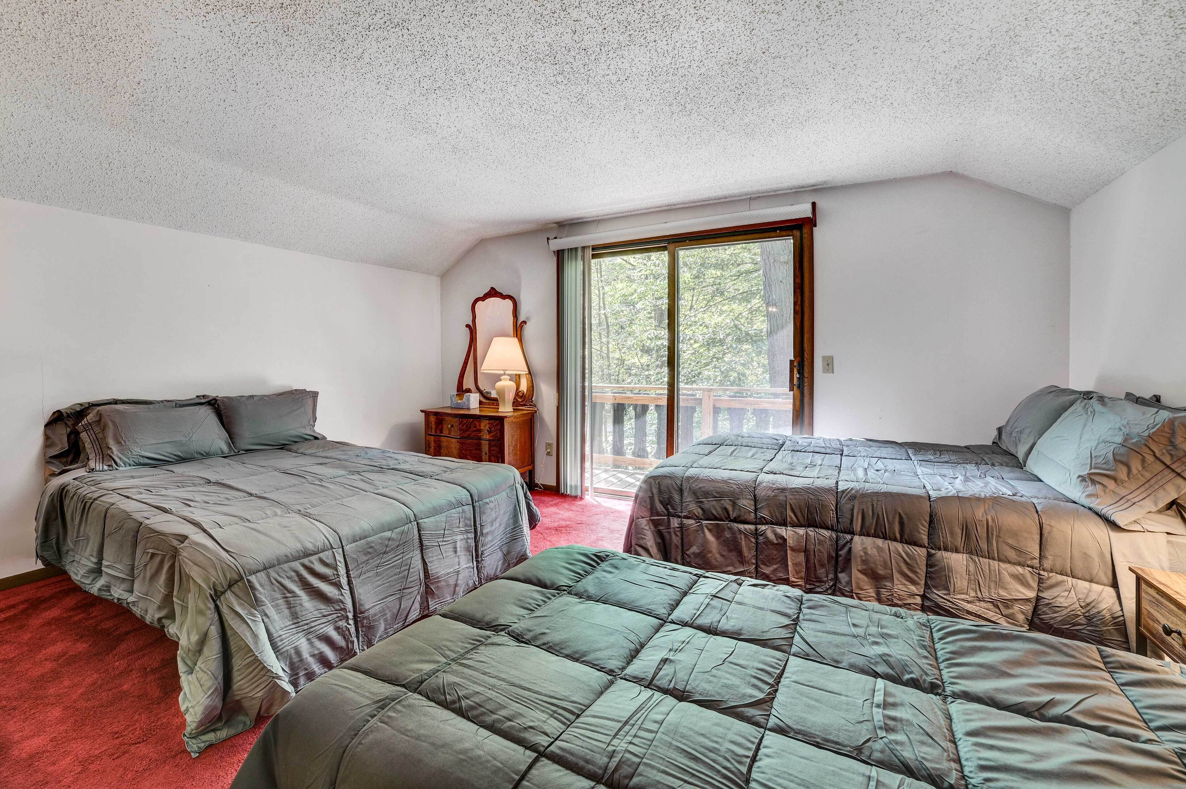 A bedroom with two beds, a nightstand, a lamp, and a window with a view of trees.
