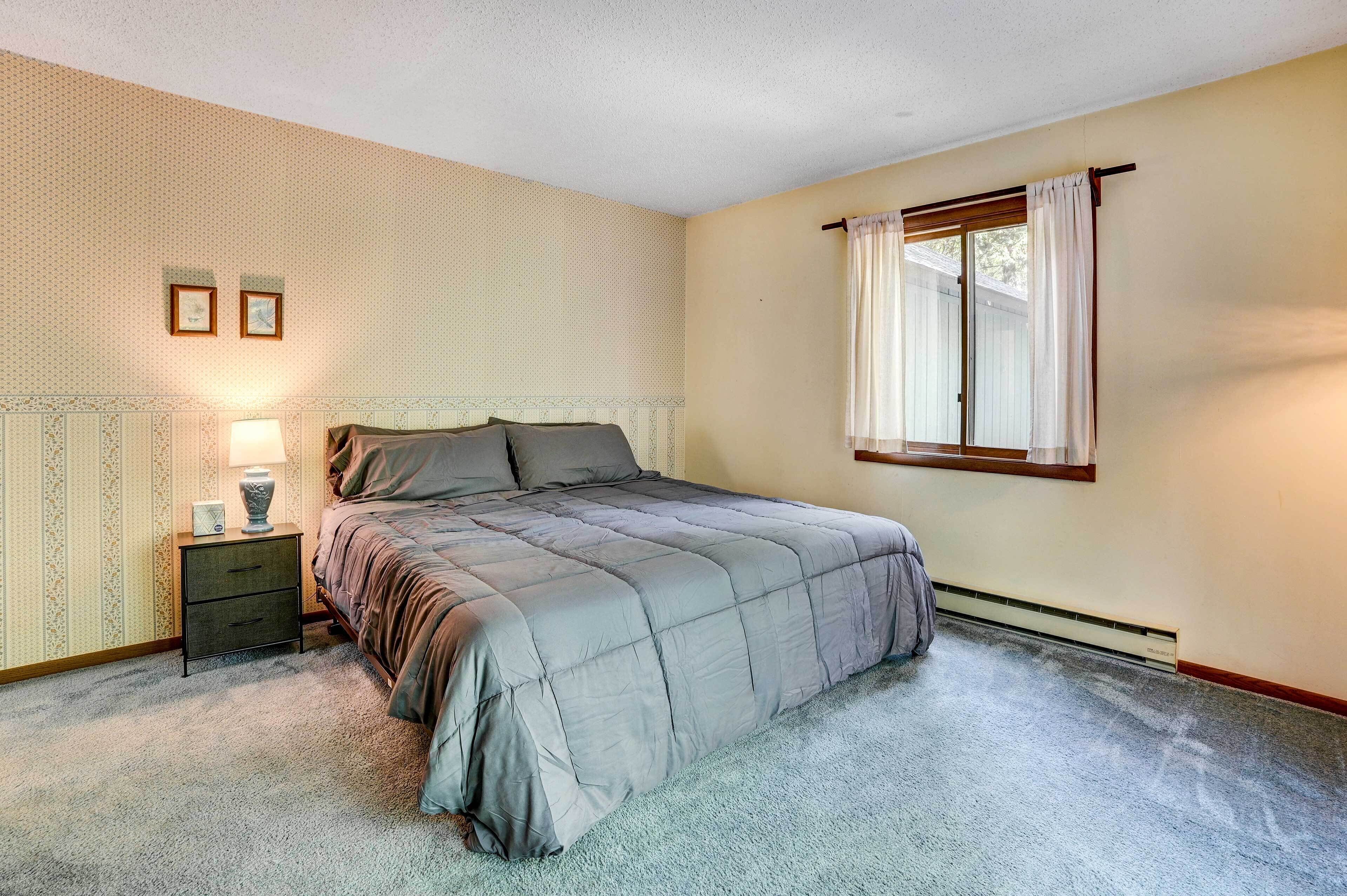 Une chambre à coucher avec un lit, une table de chevet, une lampe et une fenêtre avec des rideaux.