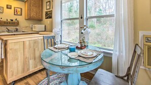 Un coin repas avec une table en verre pour quatre personnes, des meubles en bois, un four à micro-ondes et une fenêtre donnant sur des arbres.