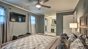 A bedroom with a large bed, a ceiling fan, a TV mounted on the wall, and a bathroom visible through an open door. - Chattanooga House Rental w/ Private Backyard! (Chattanooga)