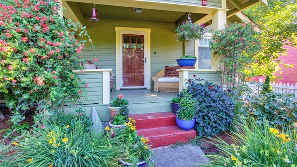 A porch with a red door, potted plants, and a wicker chair. - Charming Eugene Vacation Home: 1 Mi to Dtwn! (Eugene)