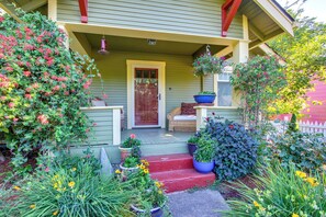 A porch with a red door, potted plants, and a wicker chair.