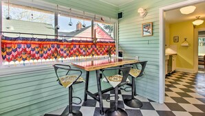 A dining area with a wooden table and four chairs, a colorful quilt hanging by the window, and a checkered floor. - Charming Eugene Vacation Home: 1 Mi to Dtwn! (Eugene)