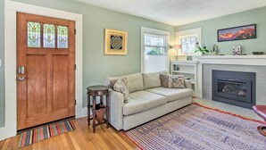 A living room with a wooden door, a sofa, a fireplace, and a patterned rug. - Charming Eugene Vacation Home: 1 Mi to Dtwn! (Eugene)