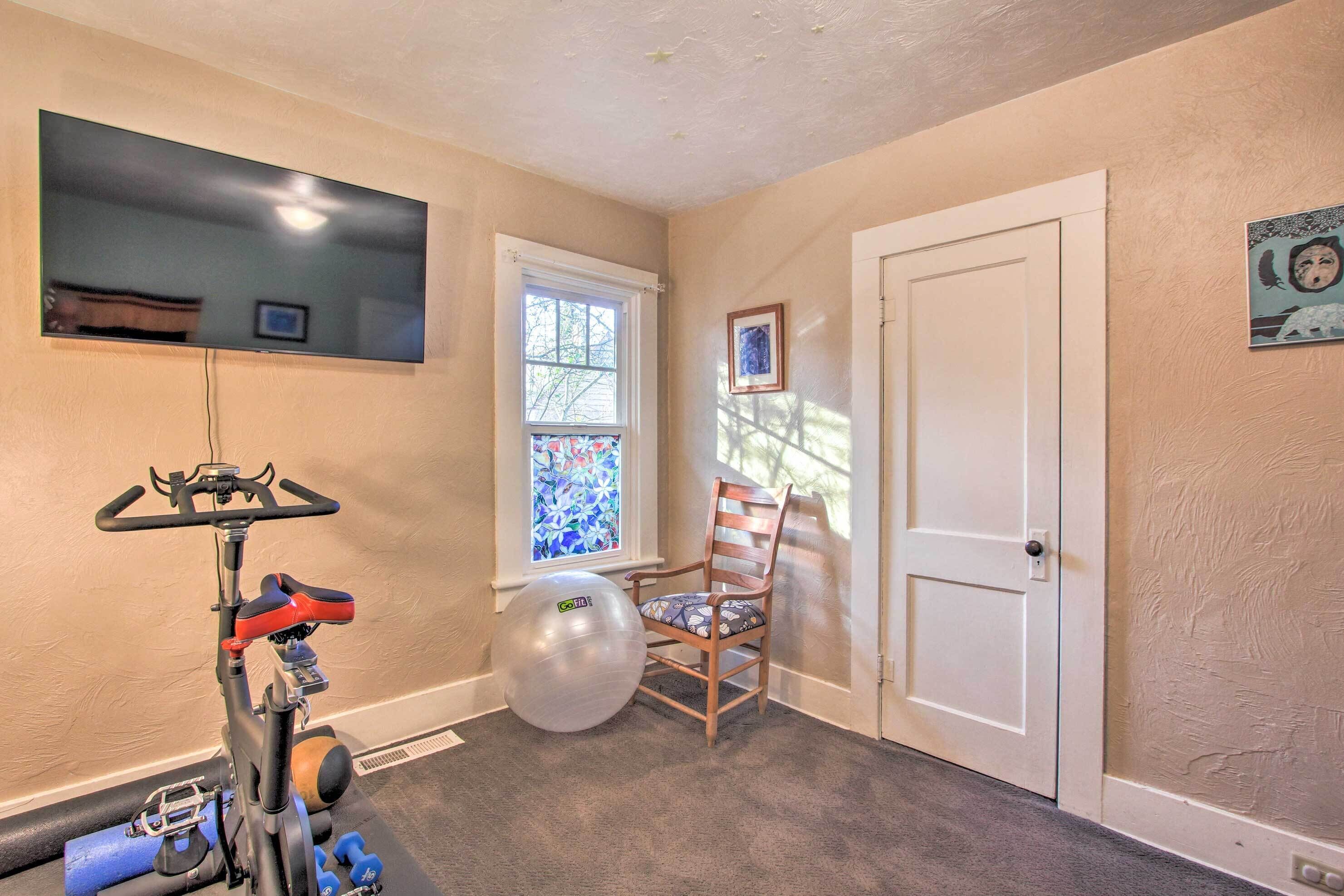 A home gym with exercise equipment, a chair, and a window with a stained glass view.