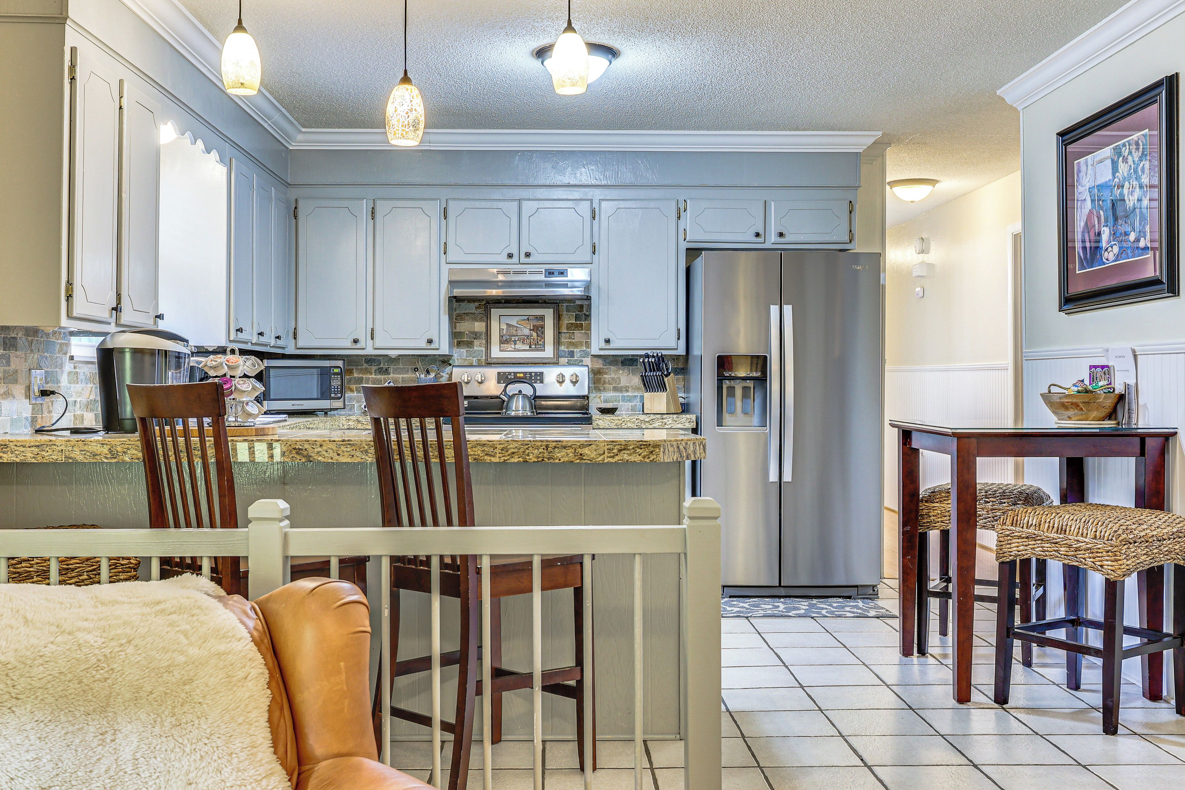 A kitchen with white cabinets, a stainless steel refrigerator, a built-in oven, and a dining area with wicker chairs.