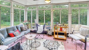 A sunroom with a ceiling fan, large windows, a grey sofa, a patterned rug, and a small table. - Sunroom & Yard: Charming Hot Springs Home! (Hot Springs)