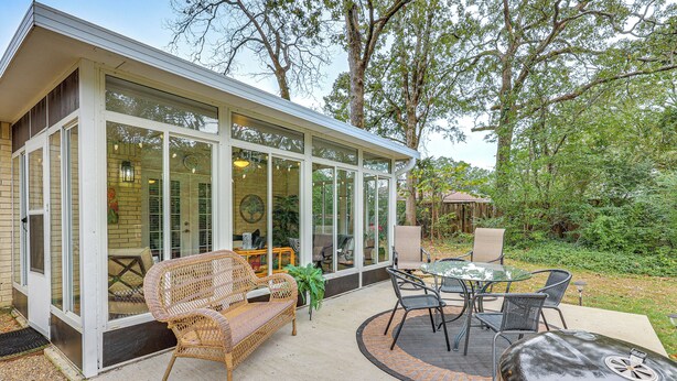 A covered patio area with wicker furniture, a grill, and a glass-enclosed room with a view of the garden. - Sunroom & Yard: Charming Hot Springs Home! (Hot Springs)