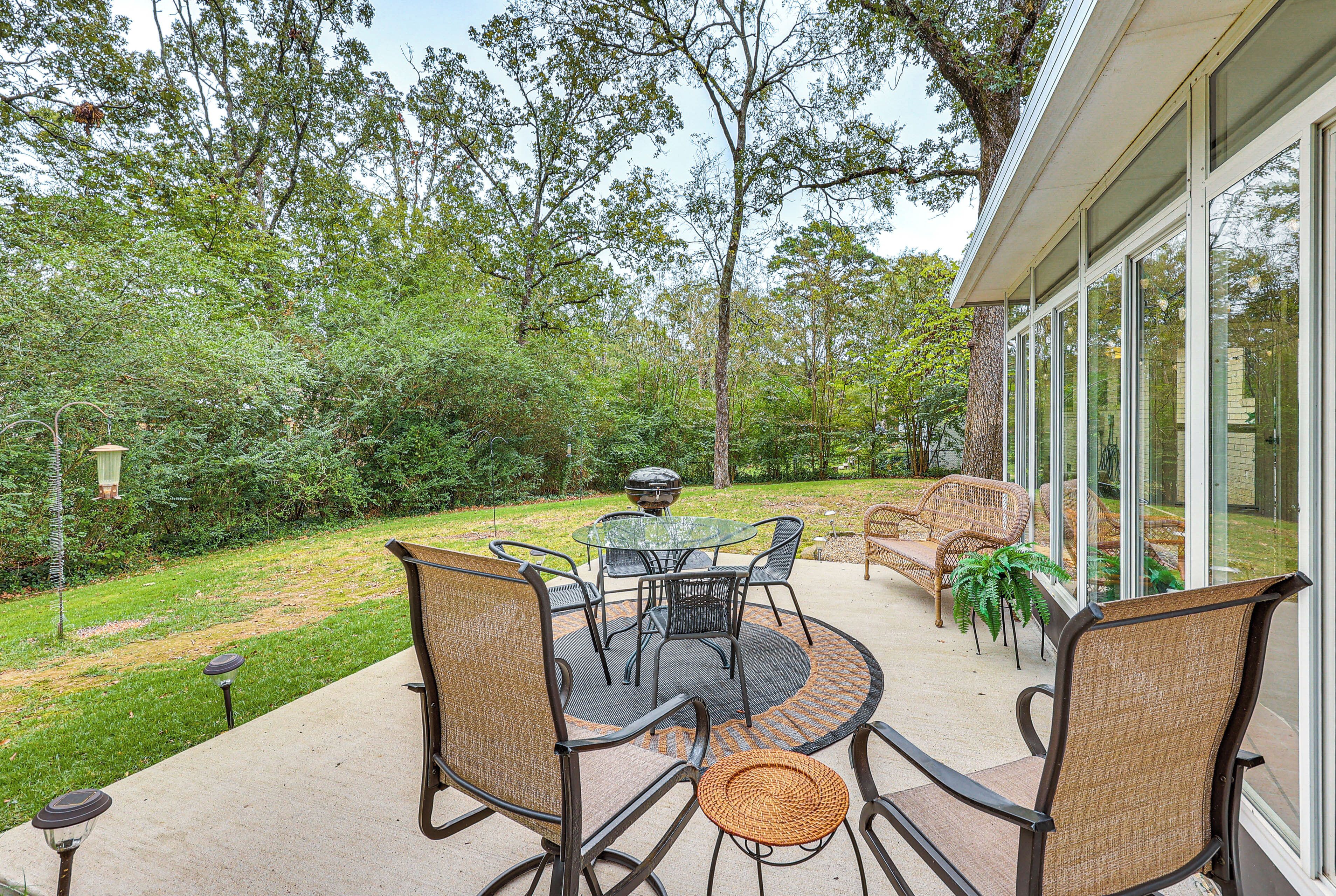 An outdoor patio with a round table and chairs, surrounded by greenery and trees.