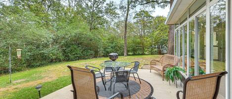 An outdoor patio with a round table and chairs, surrounded by greenery and trees.