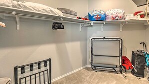 Ein kleiner, ordentlicher Raum mit einem Etagenbett, einem Stauraumregal mit diversen Gegenständen, einem Babygitter und einem Kinderwagen.