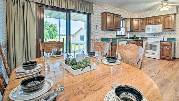 Un coin repas avec une table en bois dressée pour quatre personnes, entourée de chaises en bois. Une grande fenêtre offre une vue sur l’extérieur.